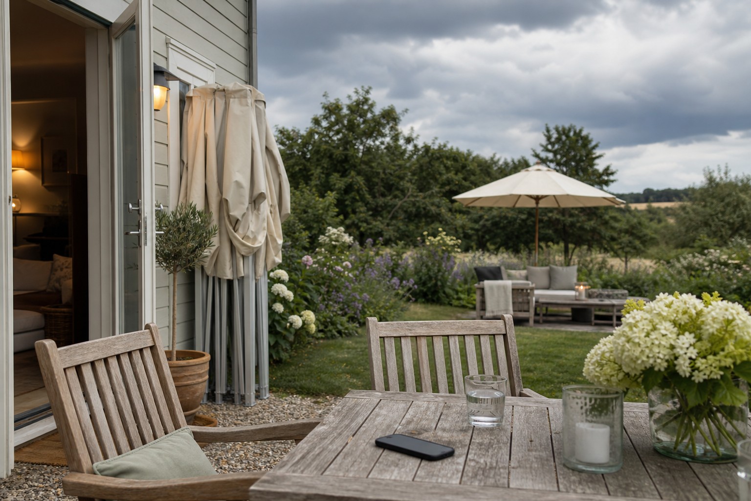 Garten mit gedecktem Tisch, offener Tür und vorbereitetem Wechsel ins Haus bei aufziehenden Wolken